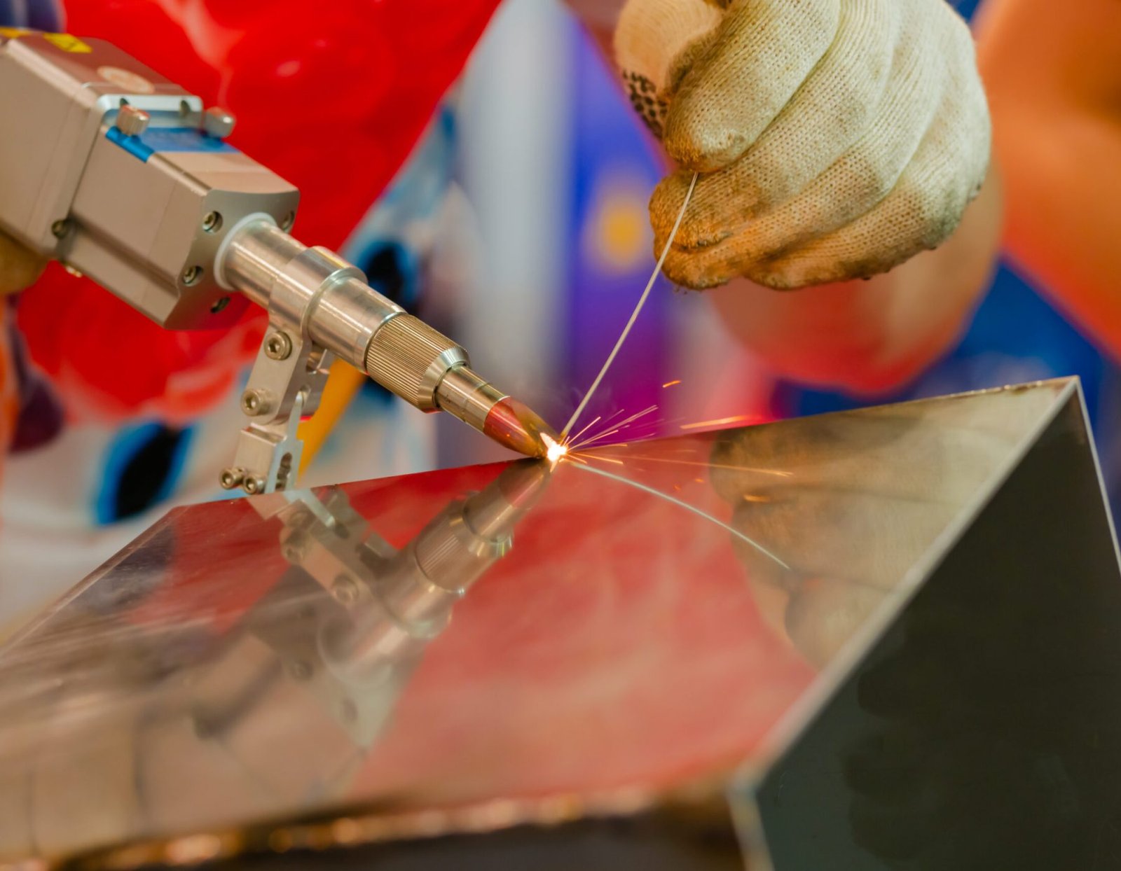 Welder hands using portable handheld laser welding machine with sparks - close up. Manufacturing, industrial, equipment, technology and metalworking concept